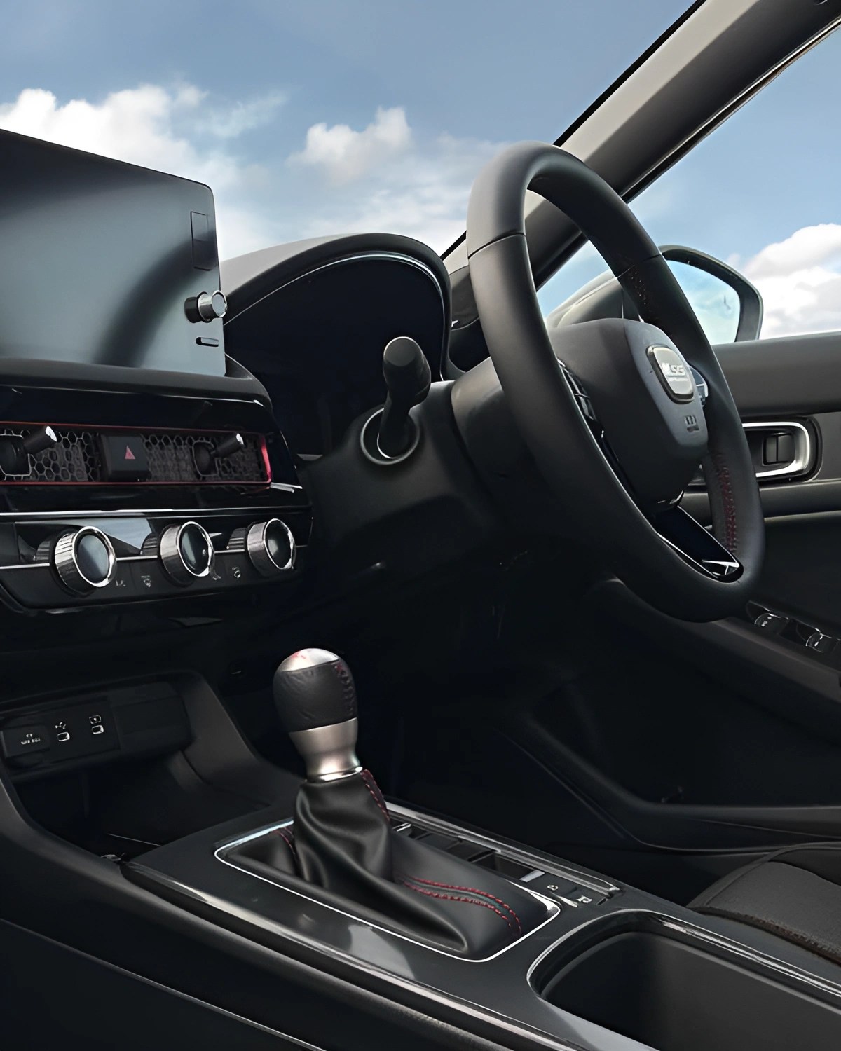 Black leather-wrapped steering wheel and gear shift lever with red stitching in a modern car interior.