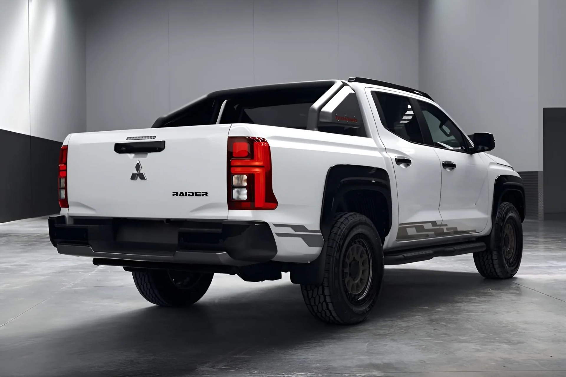 White Mitsubishi Raider pickup truck with black accents and off-road tires in a gray indoor space.