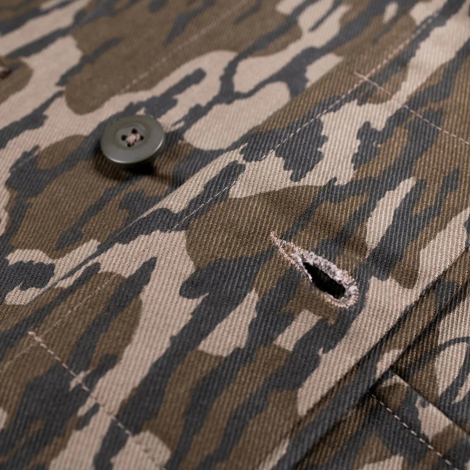 Close-up of a brown and beige camouflage fabric with a button and a stitched buttonhole.