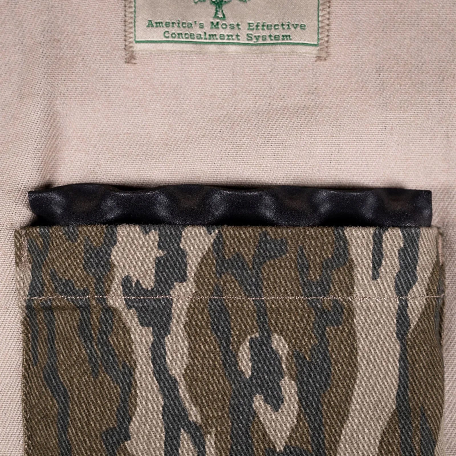 Close-up of a camouflage fabric pocket on beige material with a black textured object partially inside.