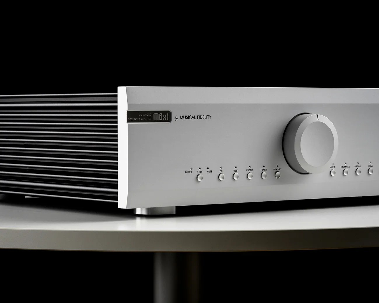 Silver Musical Fidelity M6xi integrated amplifier with multiple buttons and a large volume knob on a white table.