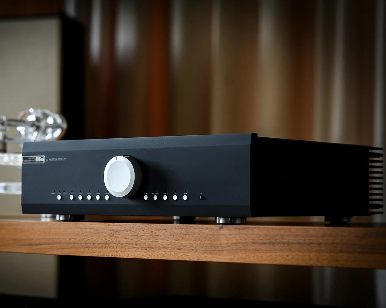 Black Musical Fidelity audio amplifier with silver volume knob and multiple input buttons on a wooden shelf.