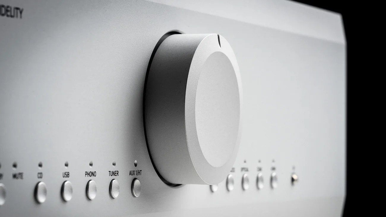 Close-up of a silver audio receiver knob with input selection buttons labeled CD, USB, PHONO, TUNER, and AUX 1/HT.