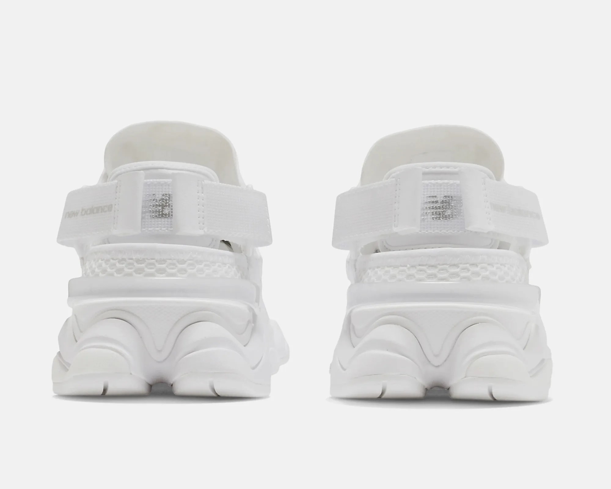 Rear view of white New Balance sneakers with textured soles and adjustable straps.