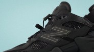 Close-up of a black New Balance sneaker with mesh panels and a reflective "N" logo on a light blue background.