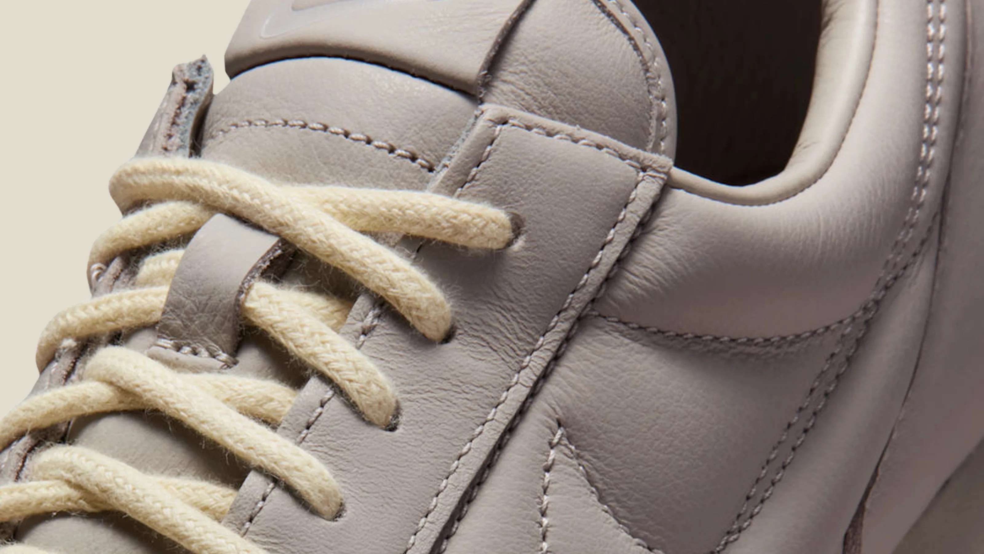 Close-up of a light gray leather sneaker with cream-colored laces and detailed stitching.