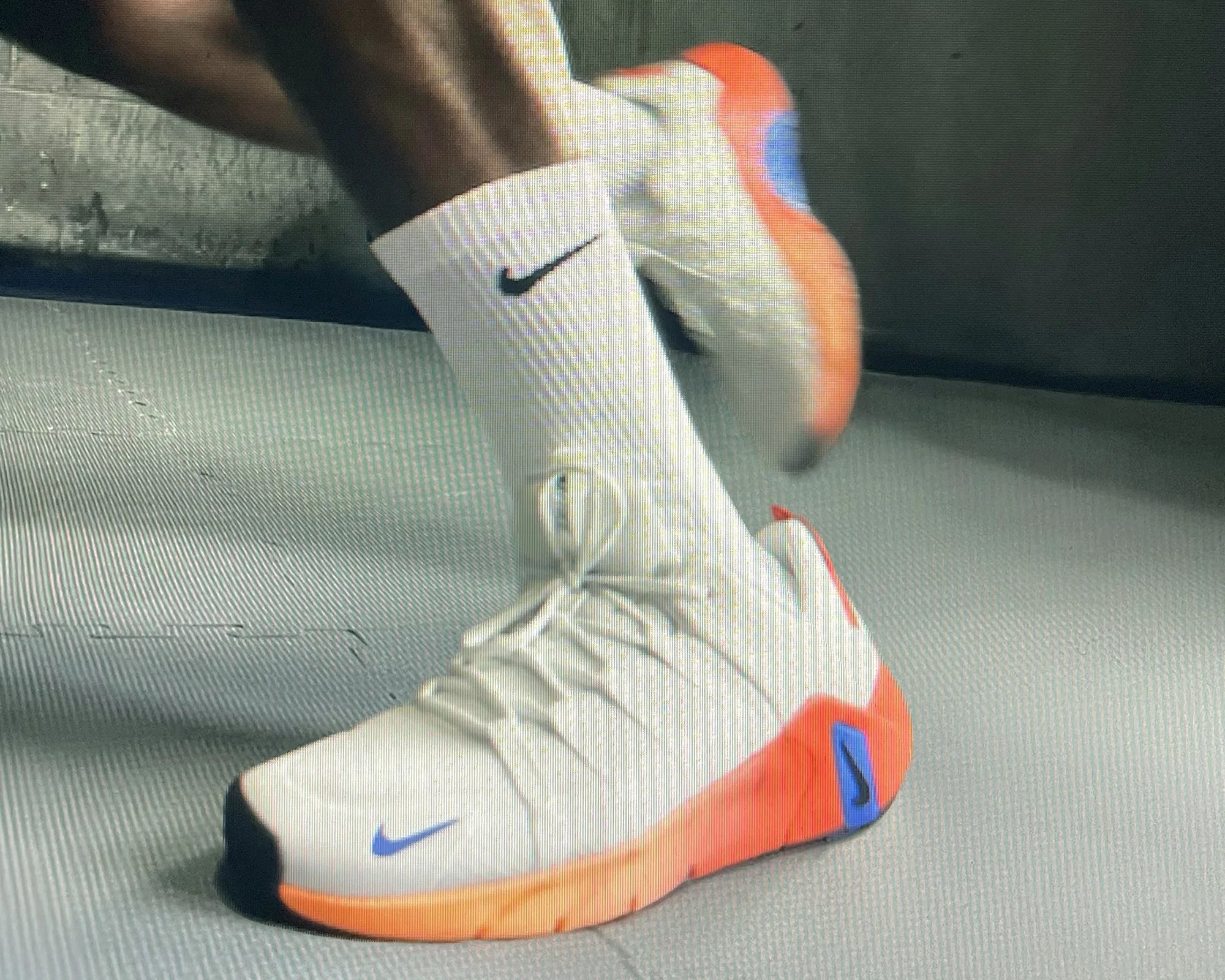 White athletic shoes with orange soles and blue Nike swooshes worn with white Nike socks.