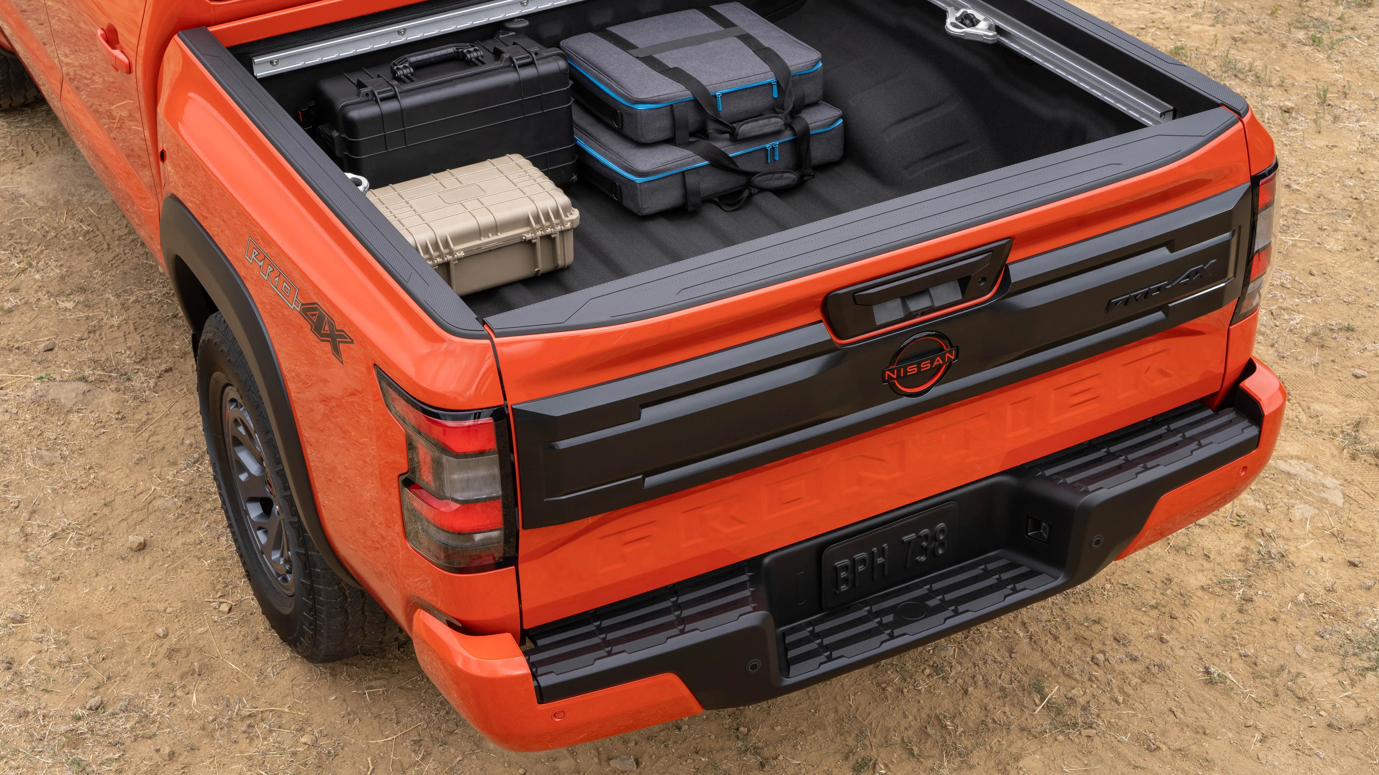 Orange Nissan Frontier Pro-4X truck bed with black and beige hard cases and gray soft cases inside.