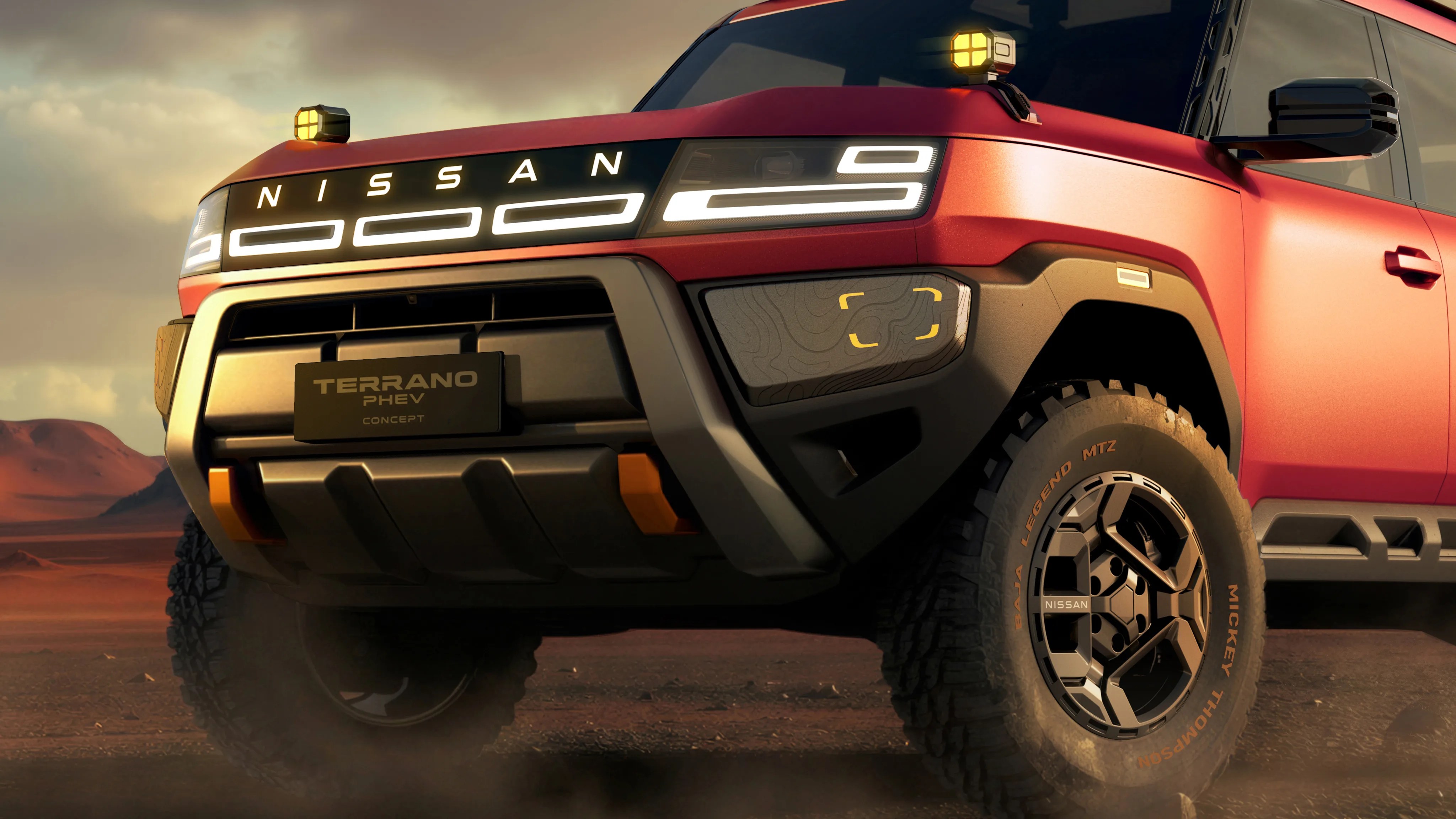 Front view of a red Nissan Terrano PHEV Concept truck with illuminated headlights and rugged tires on a dusty terrain.