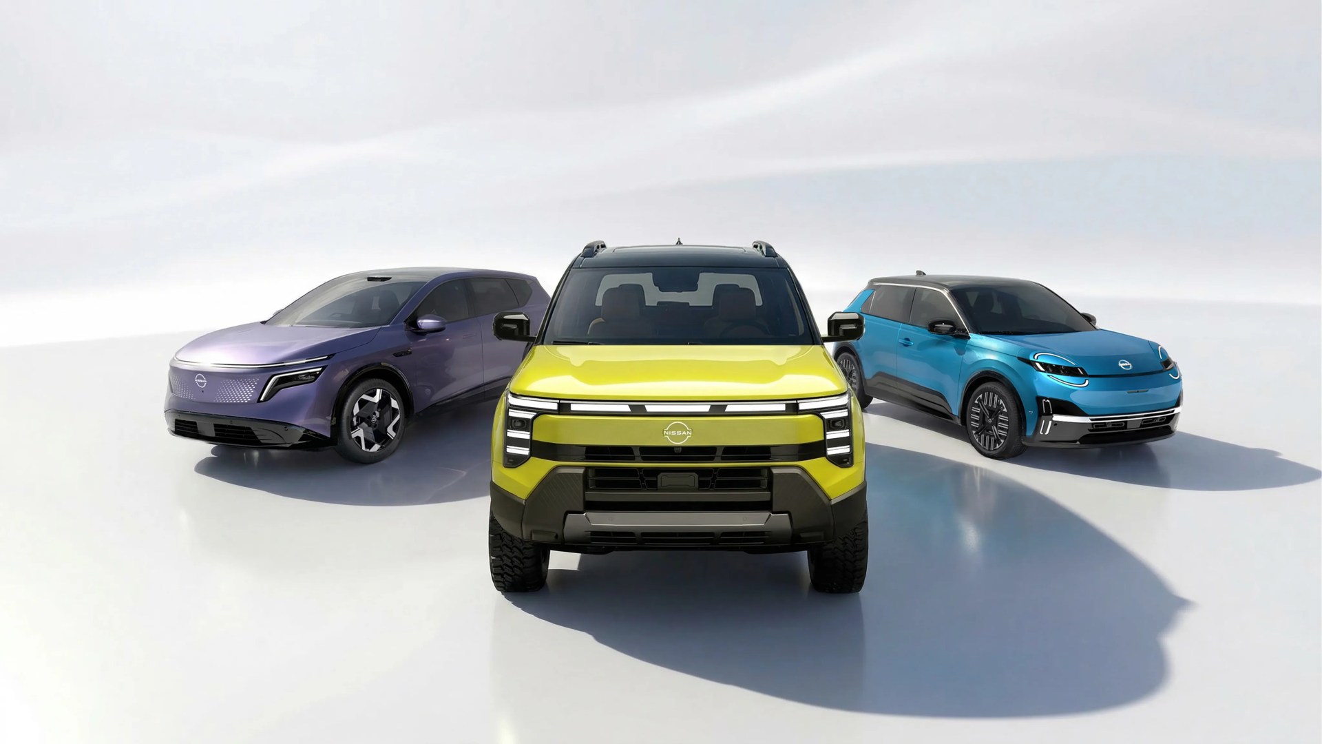 Three Nissan electric vehicles in yellow, purple, and blue, shown front-facing on a white reflective surface.