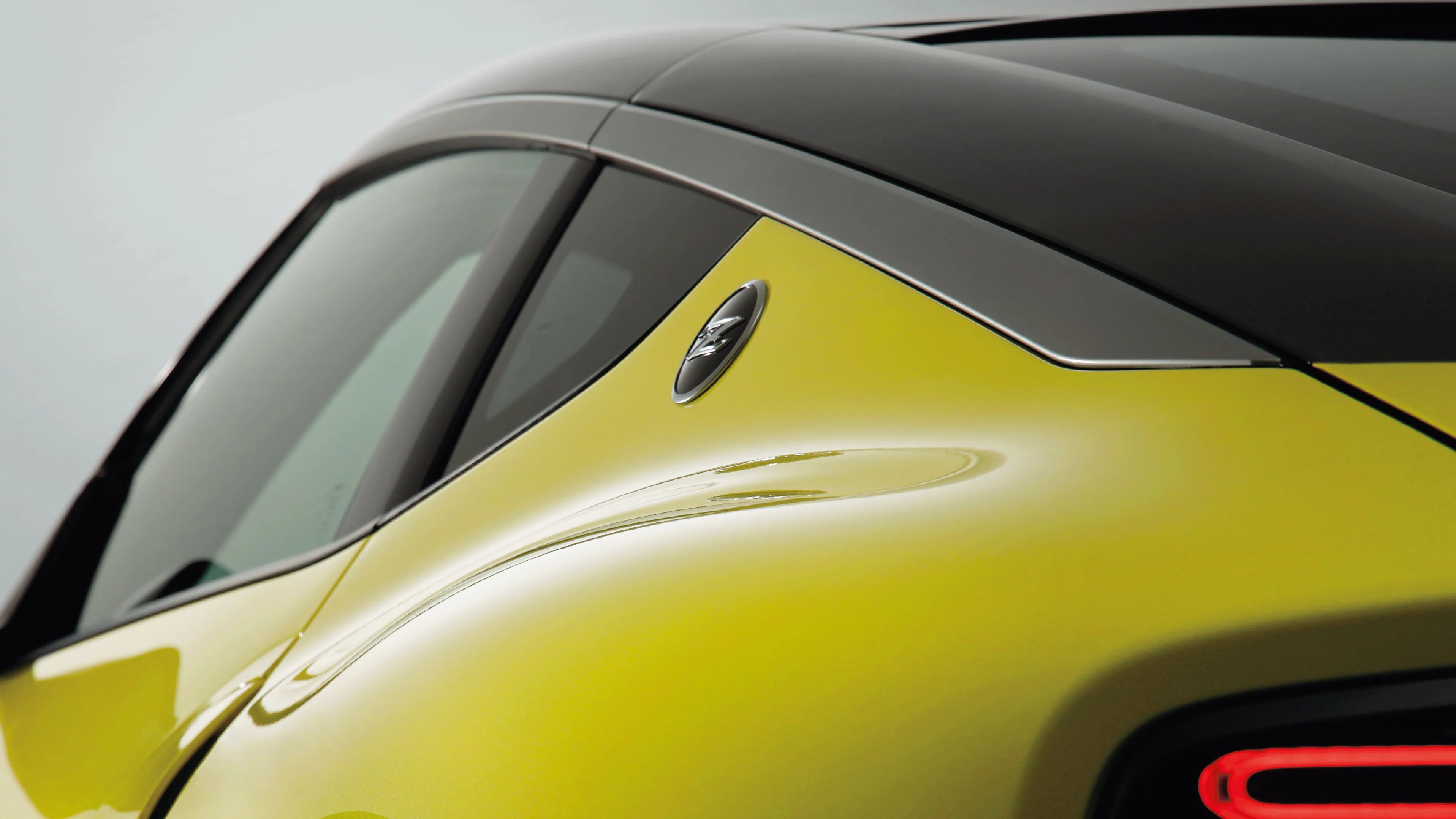 Close-up of a yellow car's rear side panel with a black roof and a small emblem near the window.