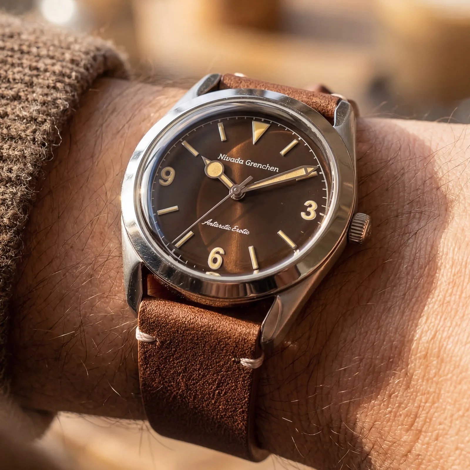 Silver wristwatch with a brown dial and beige markers on a brown leather strap worn on a wrist.
