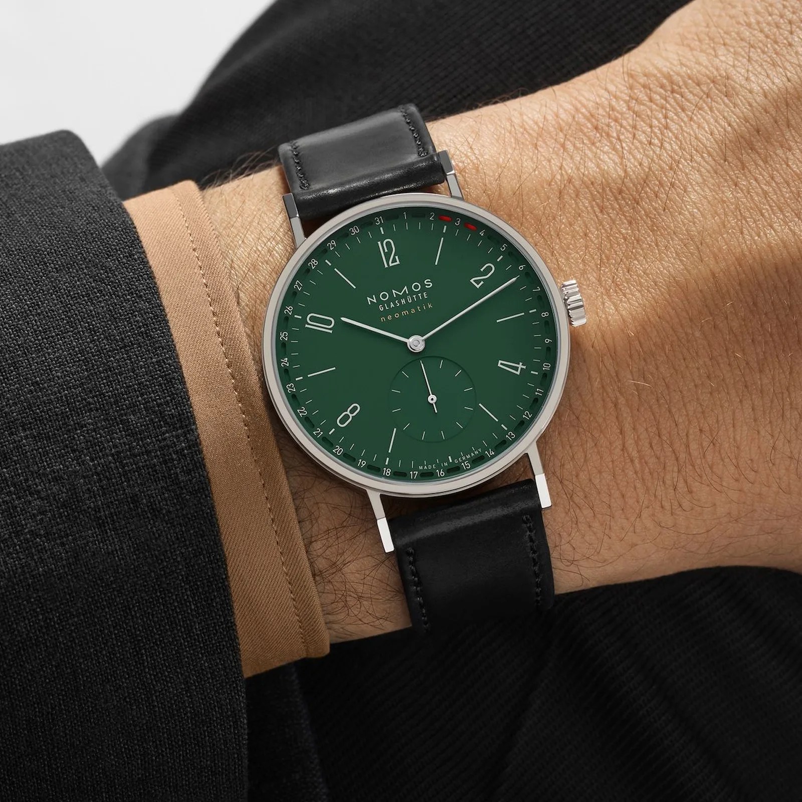 Silver Nomos Glashütte watch with dark green dial and black leather strap worn on a wrist.