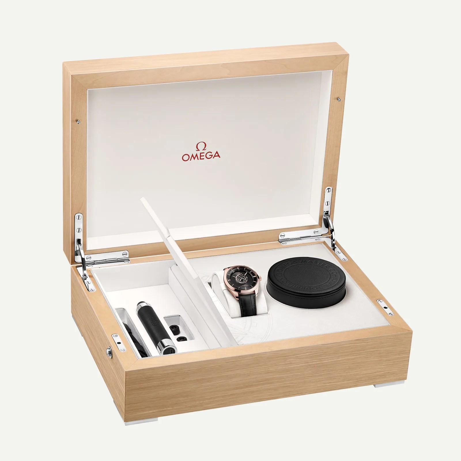 Light wood Omega watch box with white interior, holding a black and rose gold watch, a black round case, and accessories.