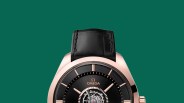 Close-up of black Omega watch face with rose gold case and black leather strap on green background.