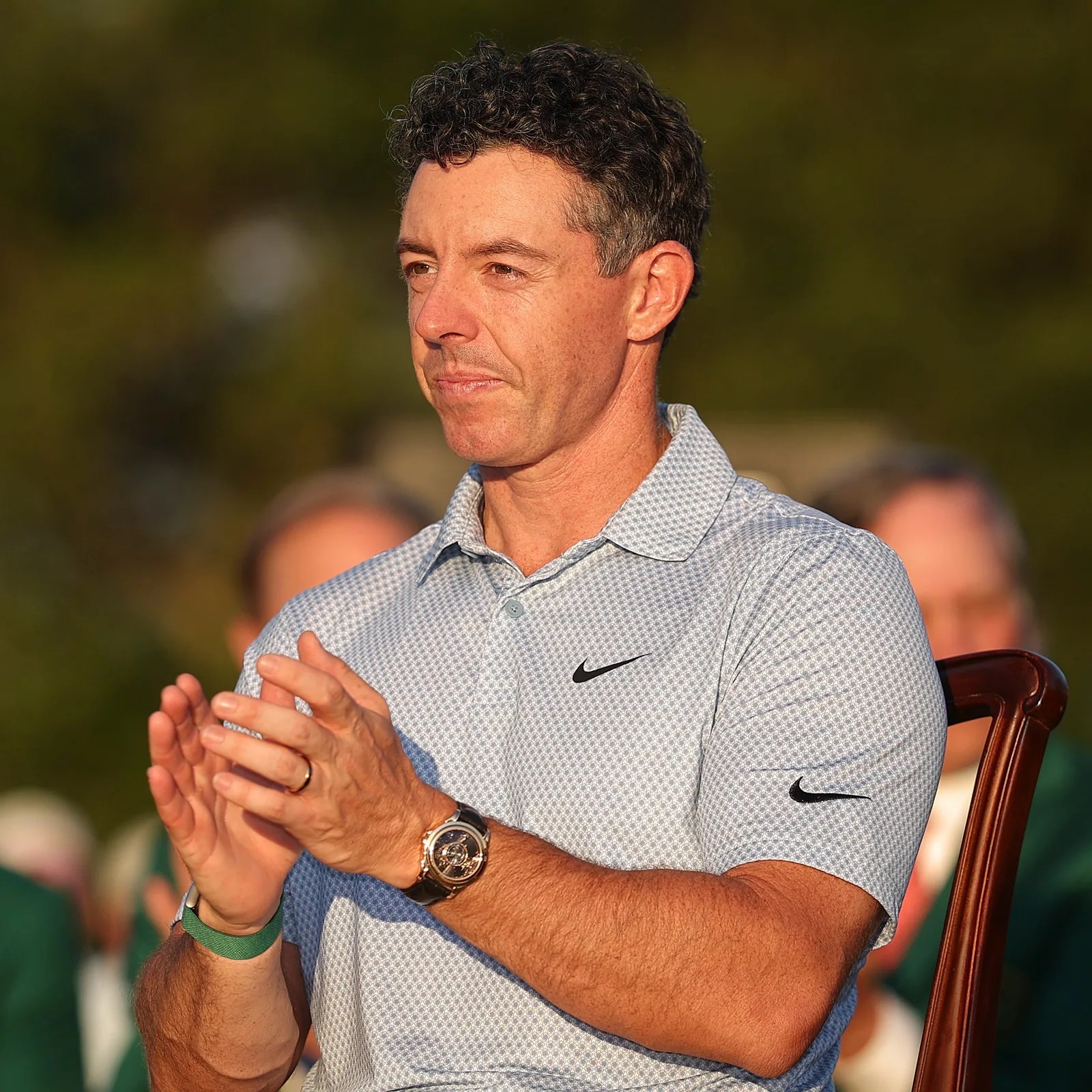 Man wearing a light blue patterned Nike polo shirt and a black wristwatch, clapping hands.