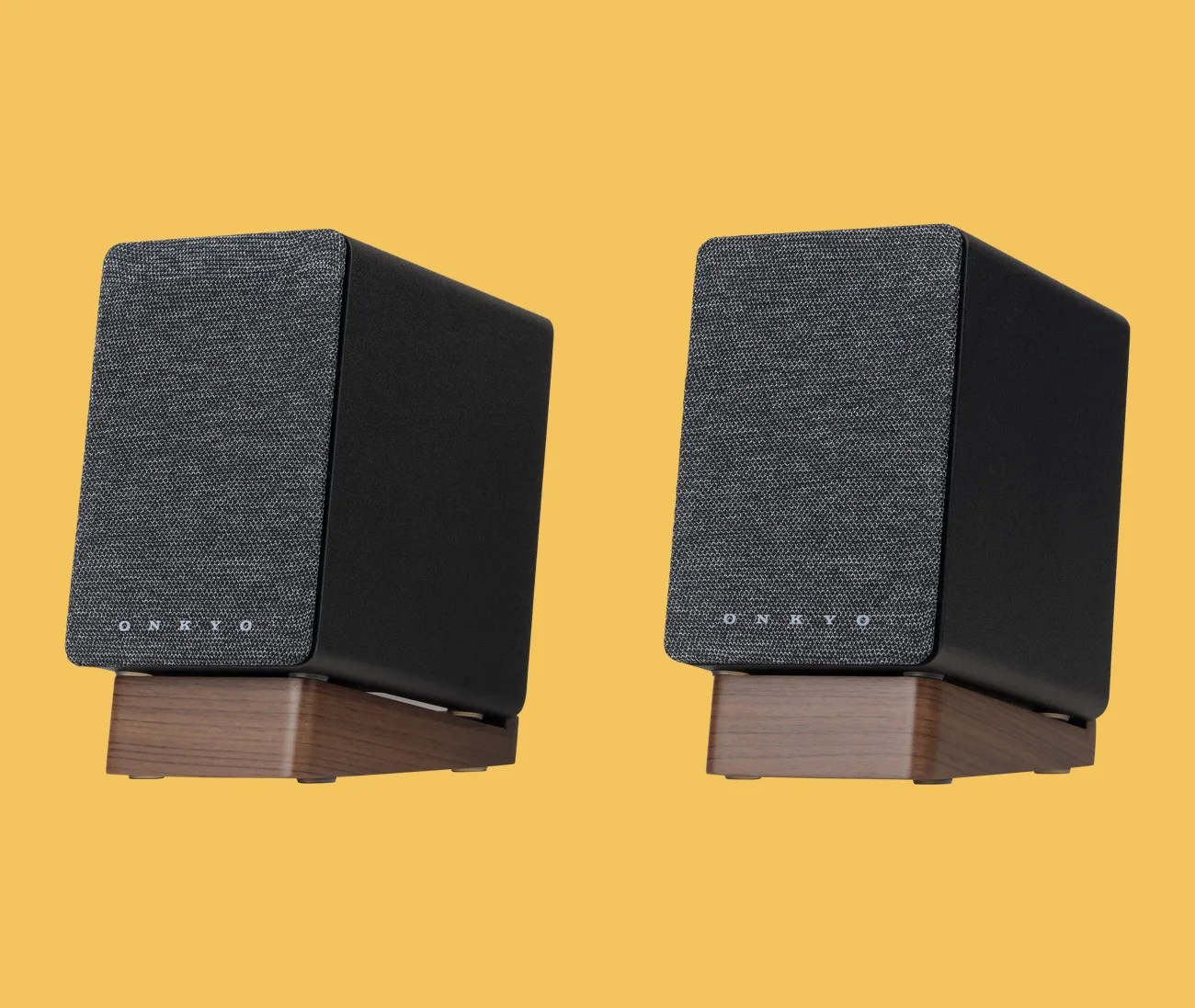 Pair of black Onkyo bookshelf speakers with gray fabric fronts and wooden bases against a yellow background.