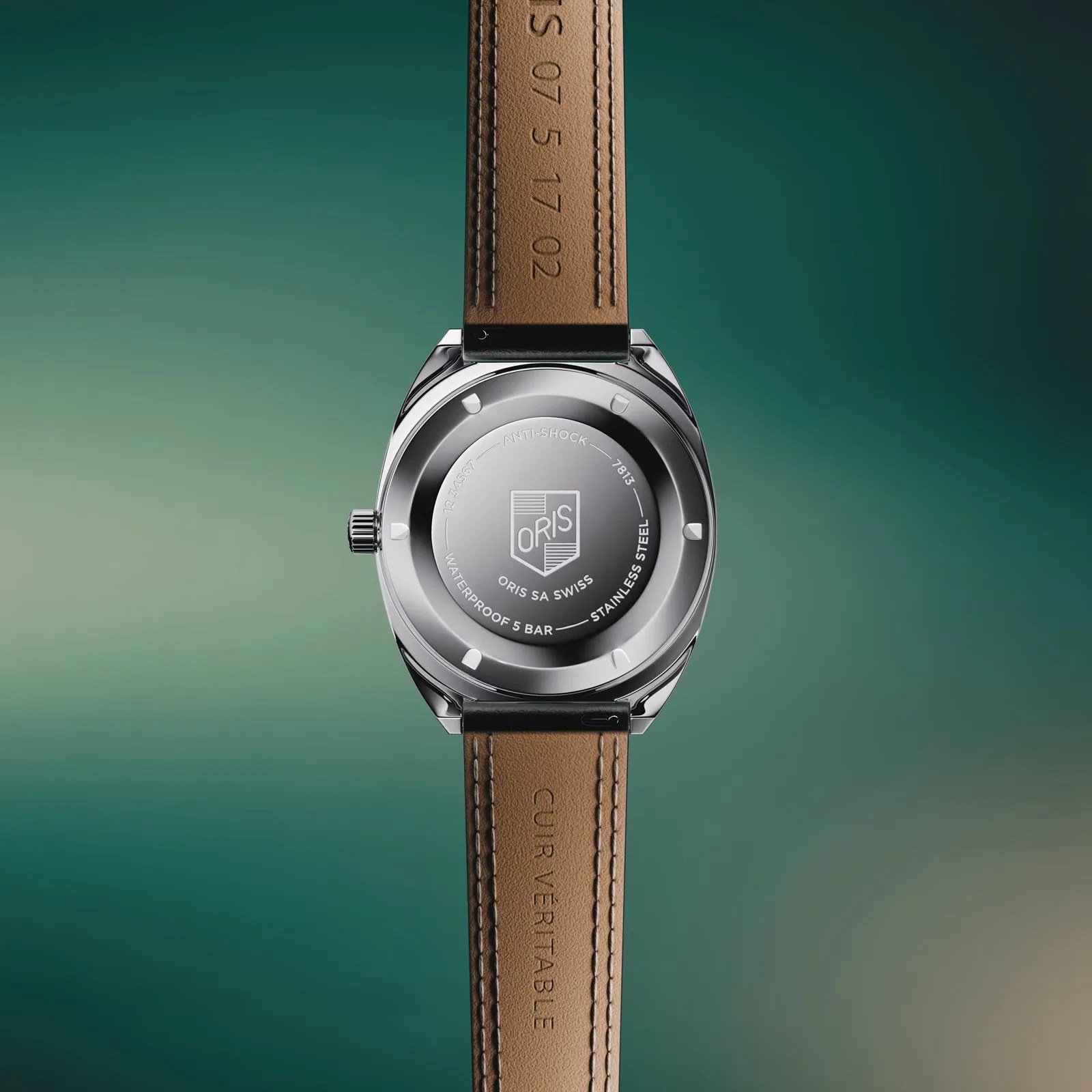 Back of a stainless steel Oris wristwatch with brown leather strap on a green gradient background.