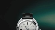 Silver Oris Star wristwatch with black leather strap and date display on a gradient dark green background.