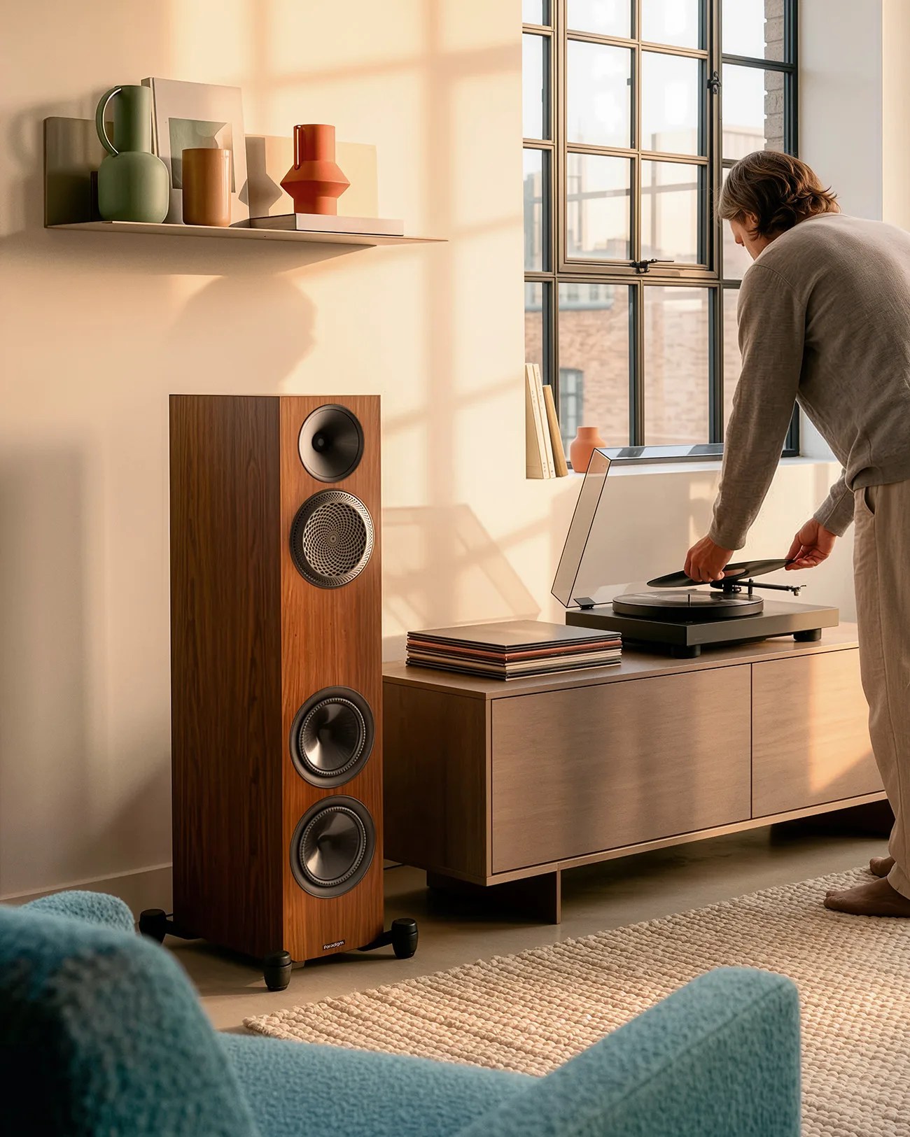 Tall wooden floor speaker with black drivers next to a wooden cabinet holding a turntable and vinyl records.