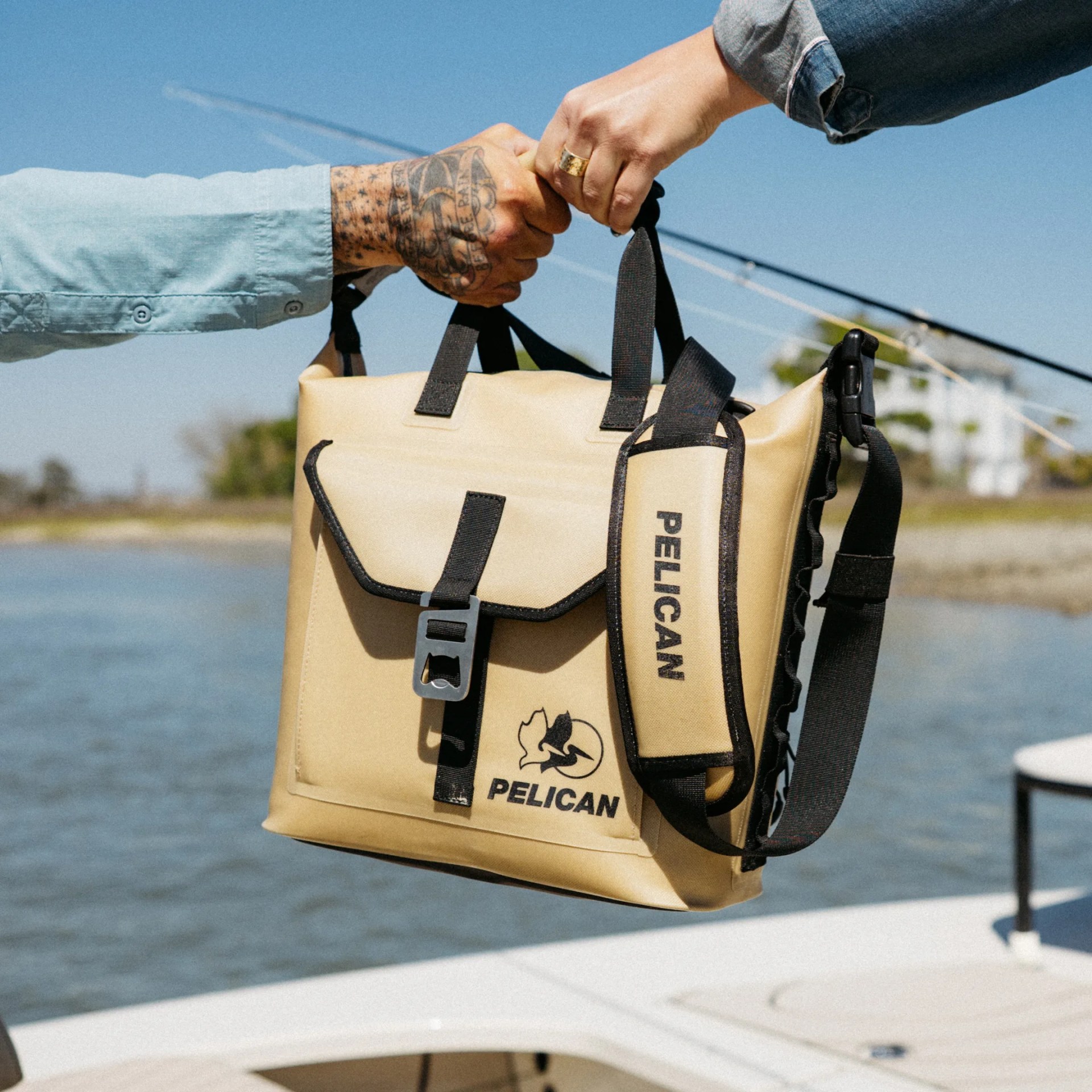 Tan Pelican waterproof bag with black straps held by two hands over a boat near water.