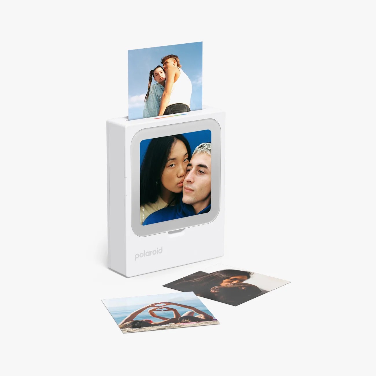 White Polaroid photo printer with a printed photo coming out and three printed photos lying in front.