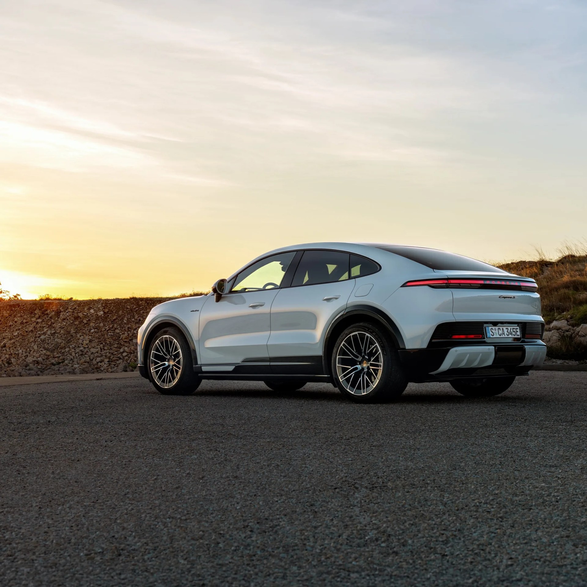 Silver Porsche Cayenne S with black wheels parked on a road at sunset.
