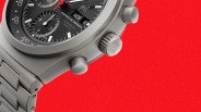 Close-up of a matte gray Porsche Design chronometer watch with black dial and red second hand on a red background.