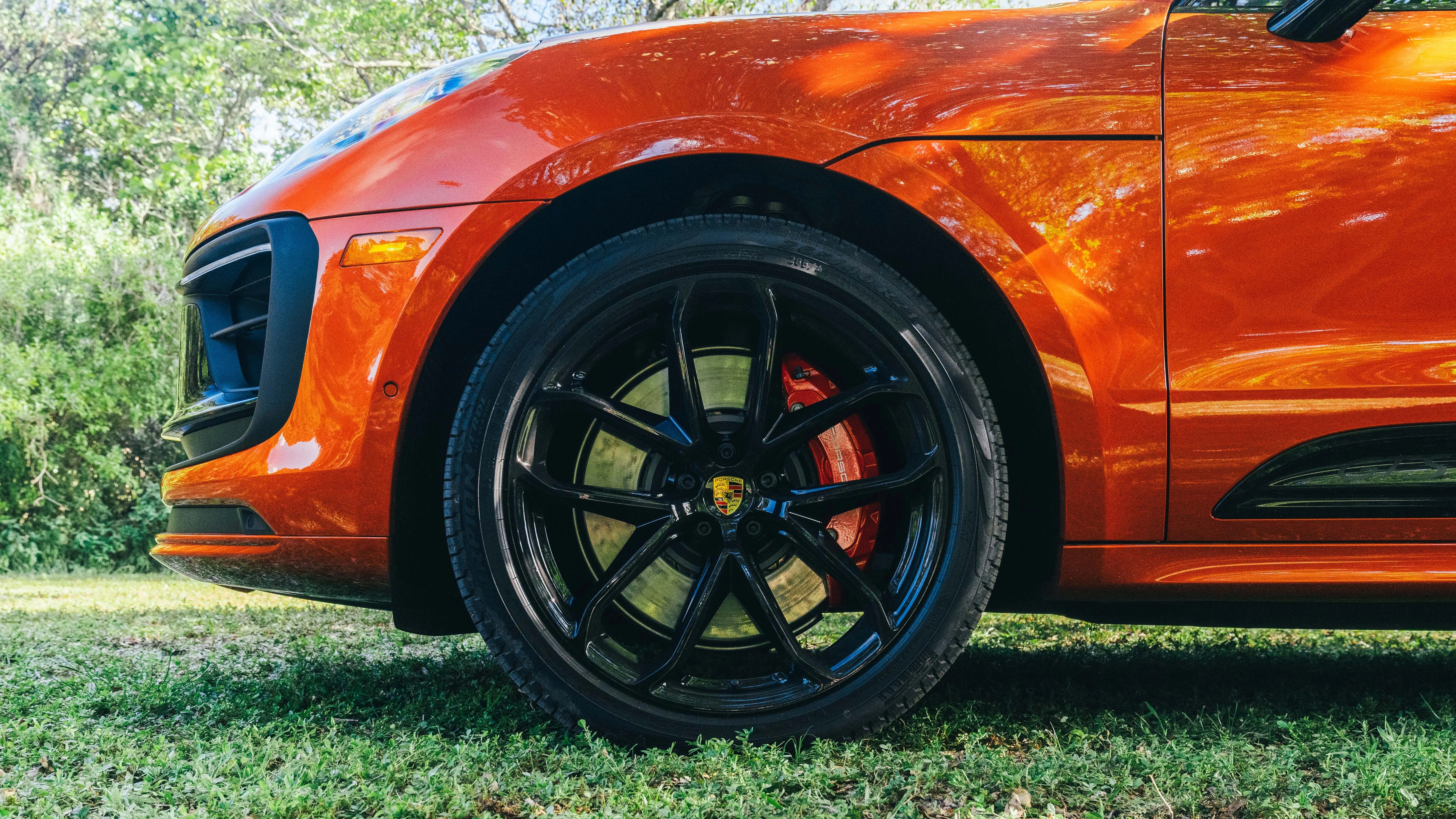 Close-up of a black alloy wheel with a red brake caliper on an orange Porsche car parked on grass.