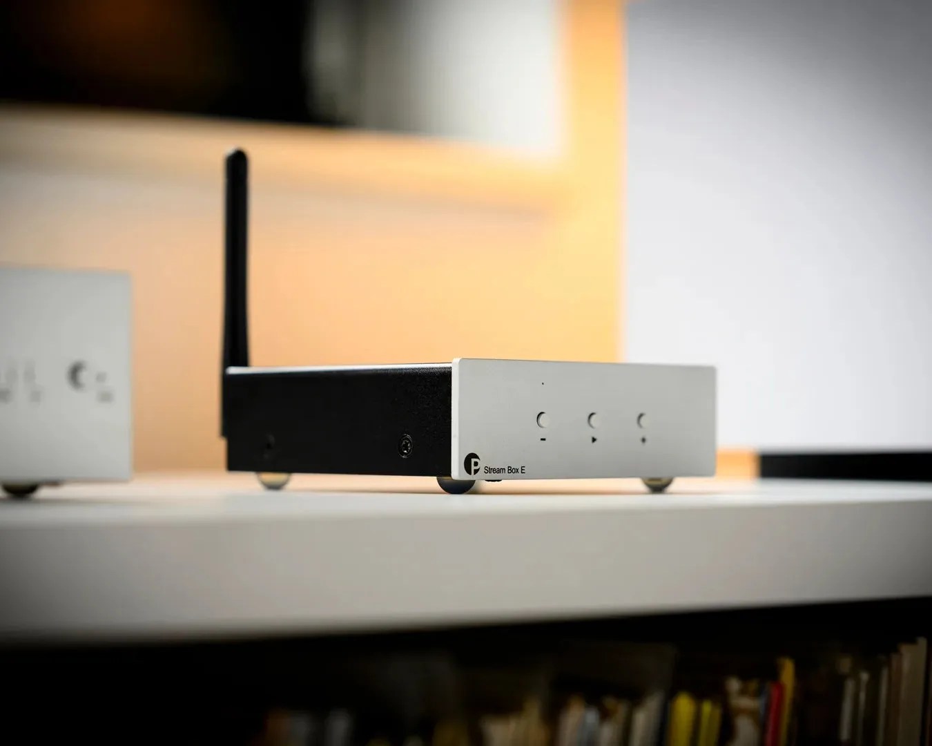 Small black and white streaming device labeled "Stream Box E" with an antenna on a white shelf.