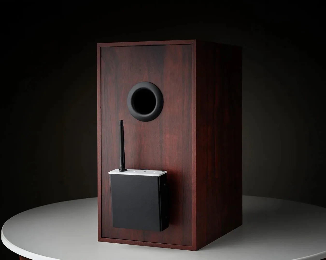 Dark wood speaker cabinet with a black wireless receiver box attached to the front and a circular port above it.