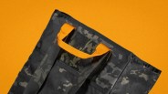 Close-up of black and gray camouflage fabric with an orange loop handle on an orange background.