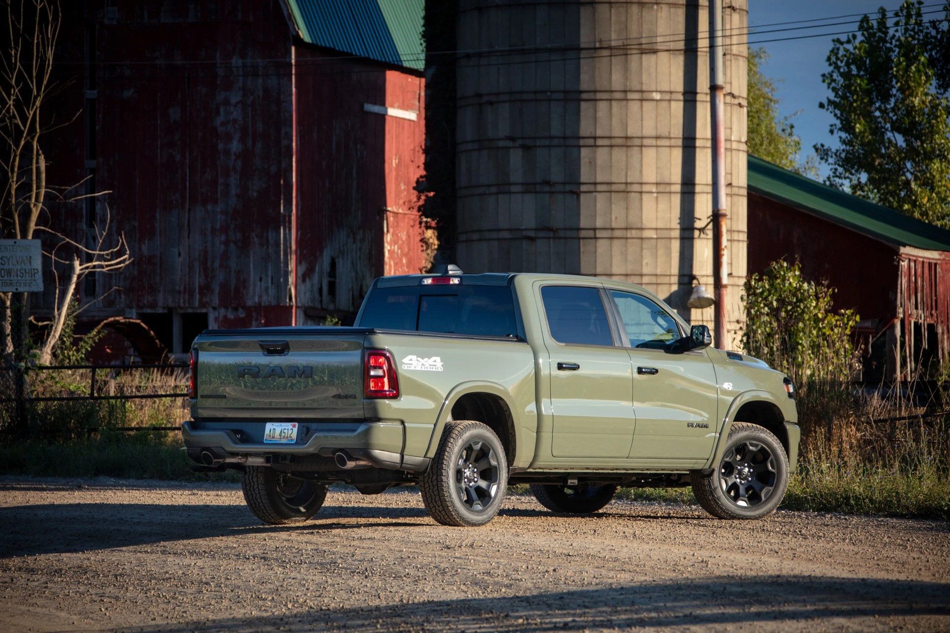 Light green RAM 4x4 off-road pickup truck parked on a dirt road near a red barn and silo.