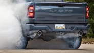 Rear view of a dark gray RAM Bighorn 4x4 pickup truck with Michigan license plate doing a burnout on asphalt.