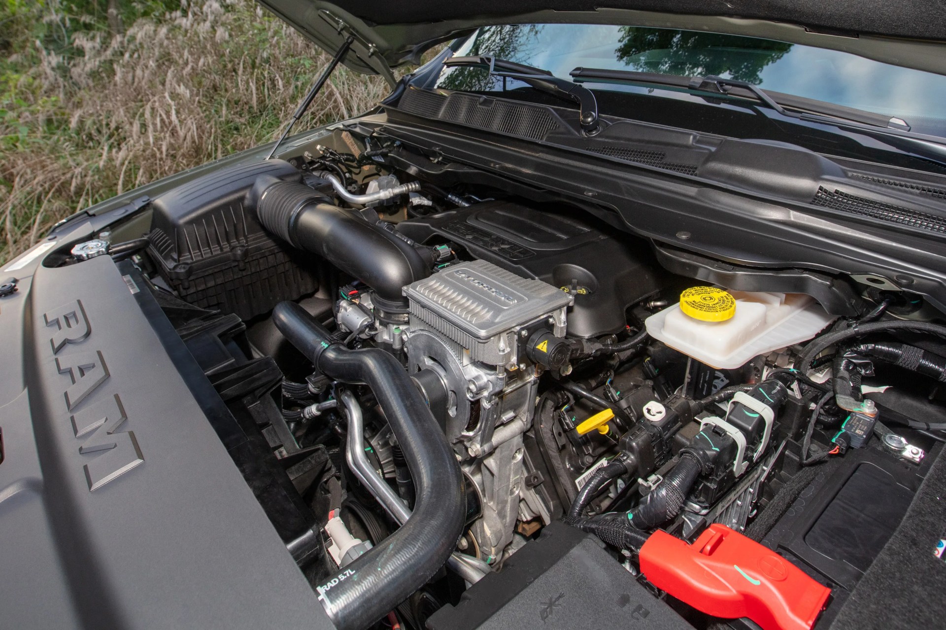 Engine compartment of a RAM vehicle showing various components including air intake, fluid reservoir with yellow cap, and battery with red cover.
