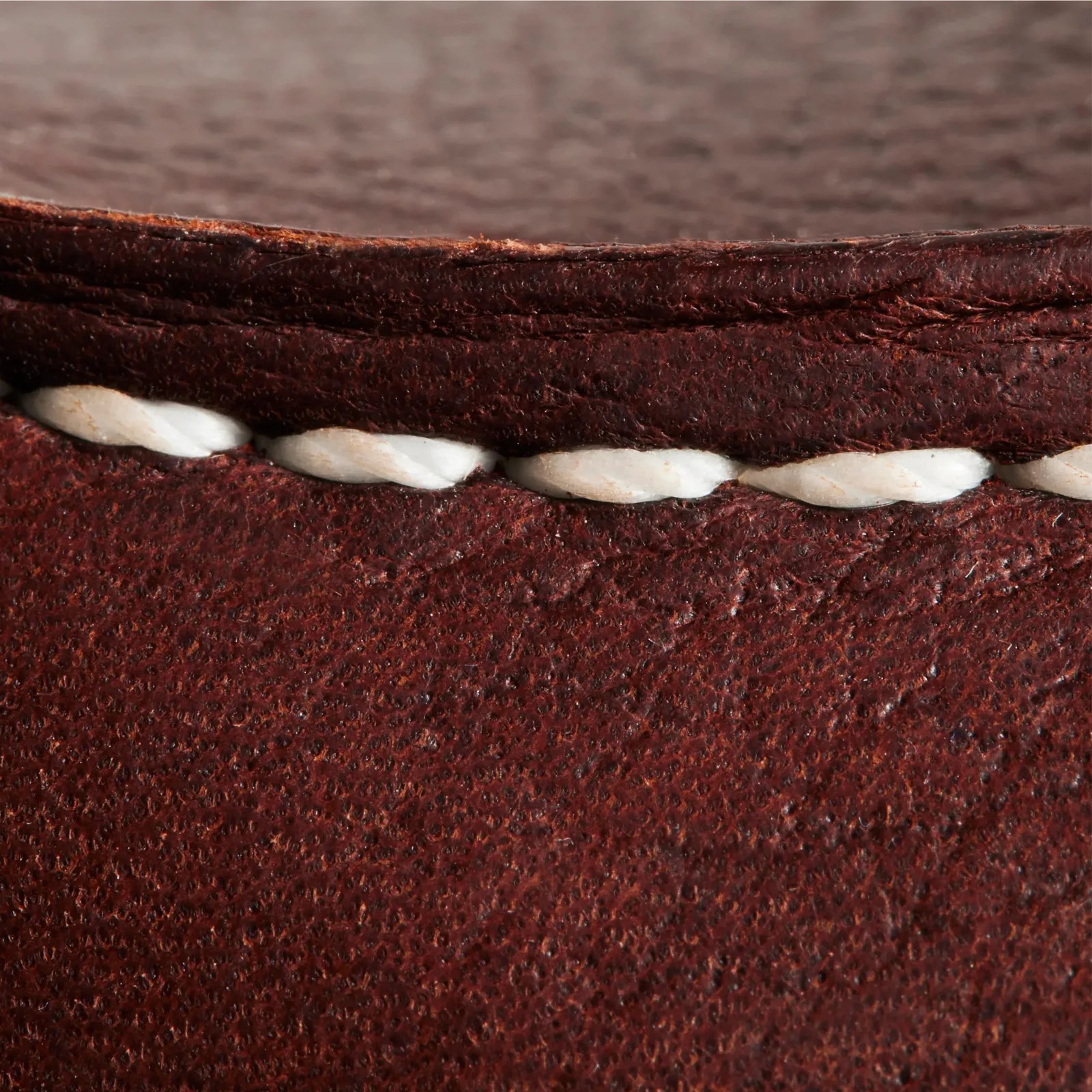 Close-up of white stitching on textured dark brown leather surface.