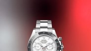 Rolex Oyster Perpetual Cosmograph Daytona watch with white dial and stainless steel bracelet against a gradient red and black background.