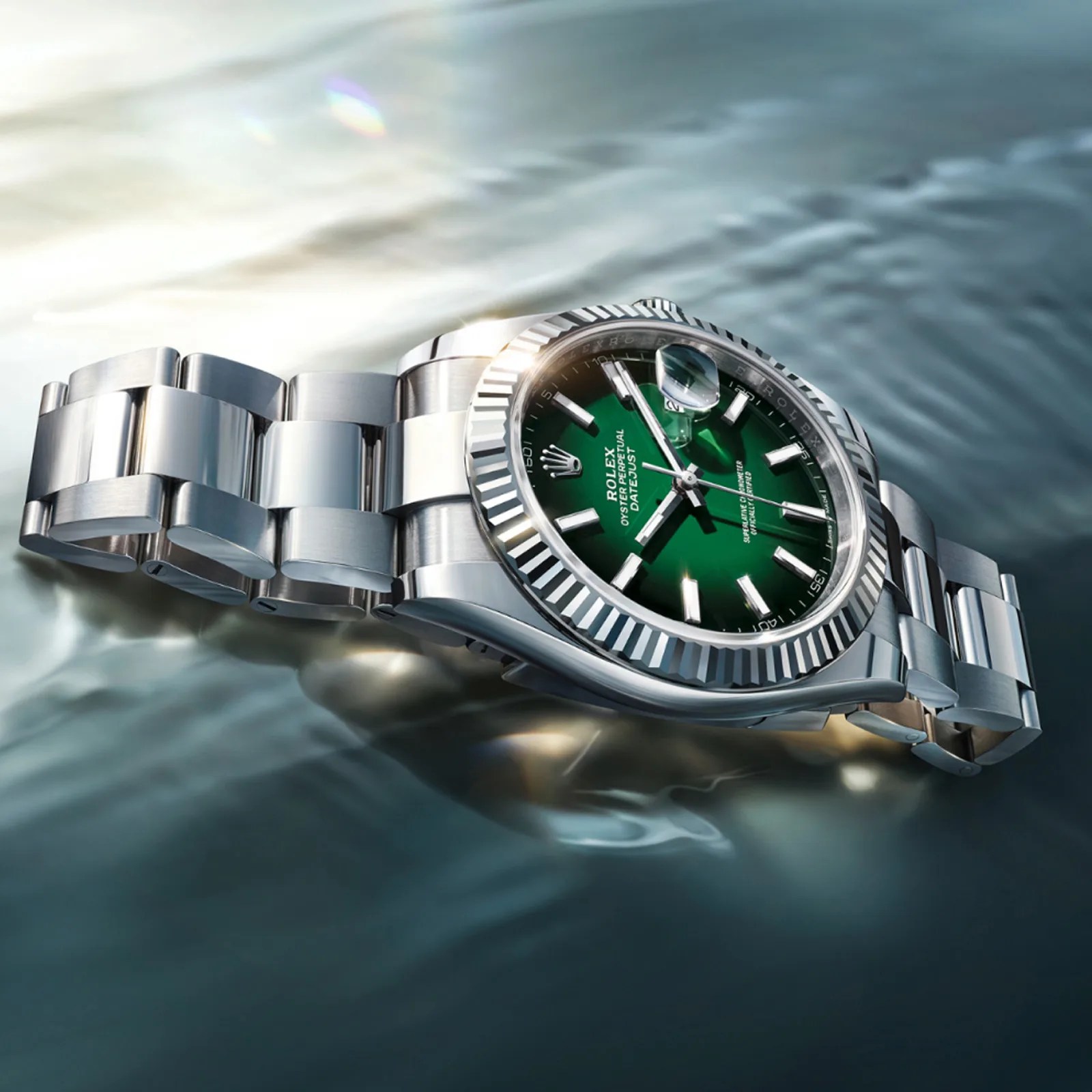 Silver Rolex Oyster Perpetual Datejust watch with a green dial and fluted bezel on water surface.