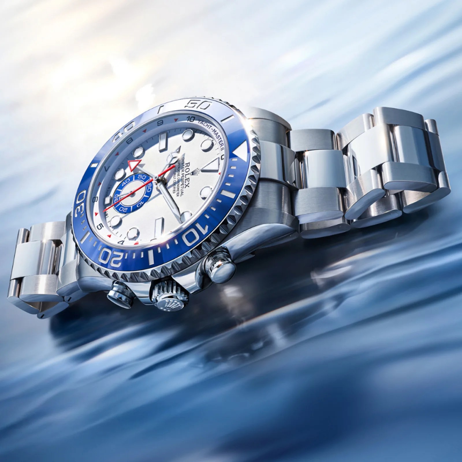 Silver Rolex Yacht-Master II watch with a white dial and blue bezel on a reflective blue surface.