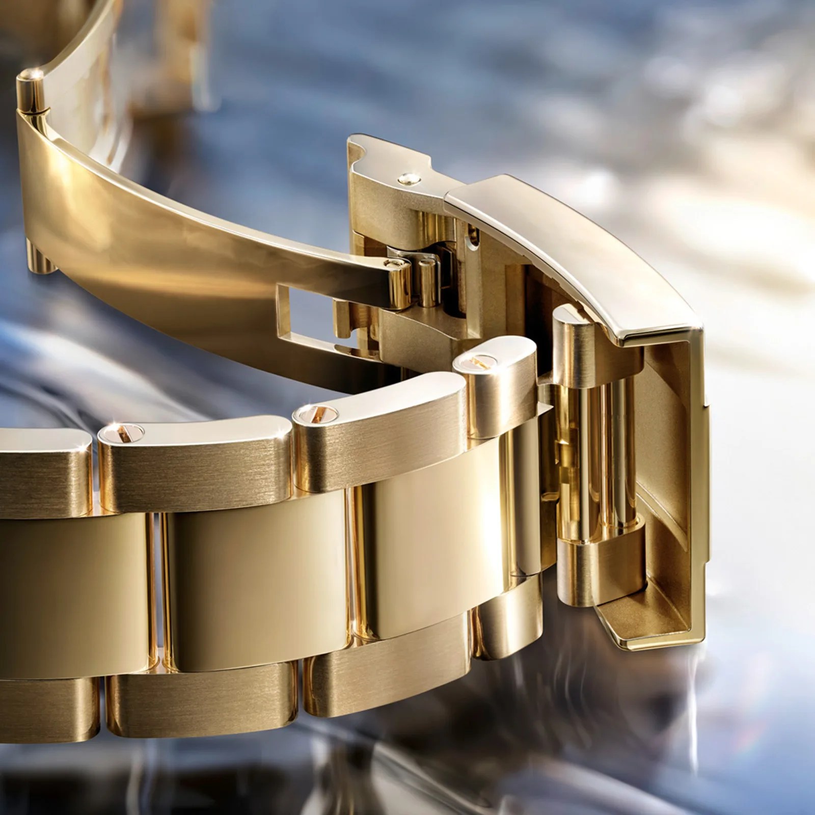 Close-up of a gold metal watch bracelet with a polished and brushed finish, showing the clasp mechanism.
