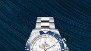 Silver Rolex Yacht-Master II watch with white dial and blue bezel on a textured dark blue surface.