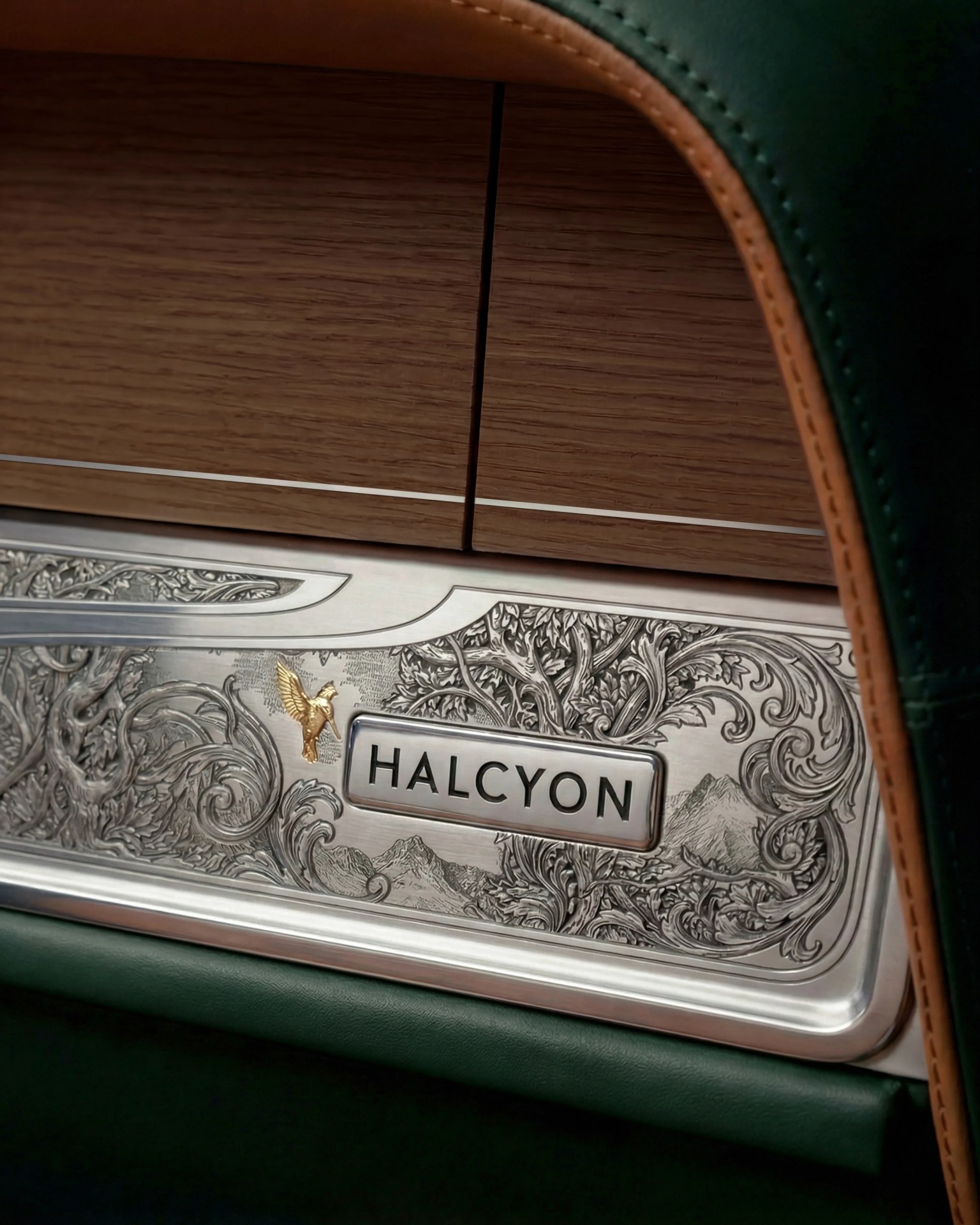 Decorative metal panel with intricate floral engravings and a gold bird emblem, labeled "HALCYON," set in a wood and leather car interior.