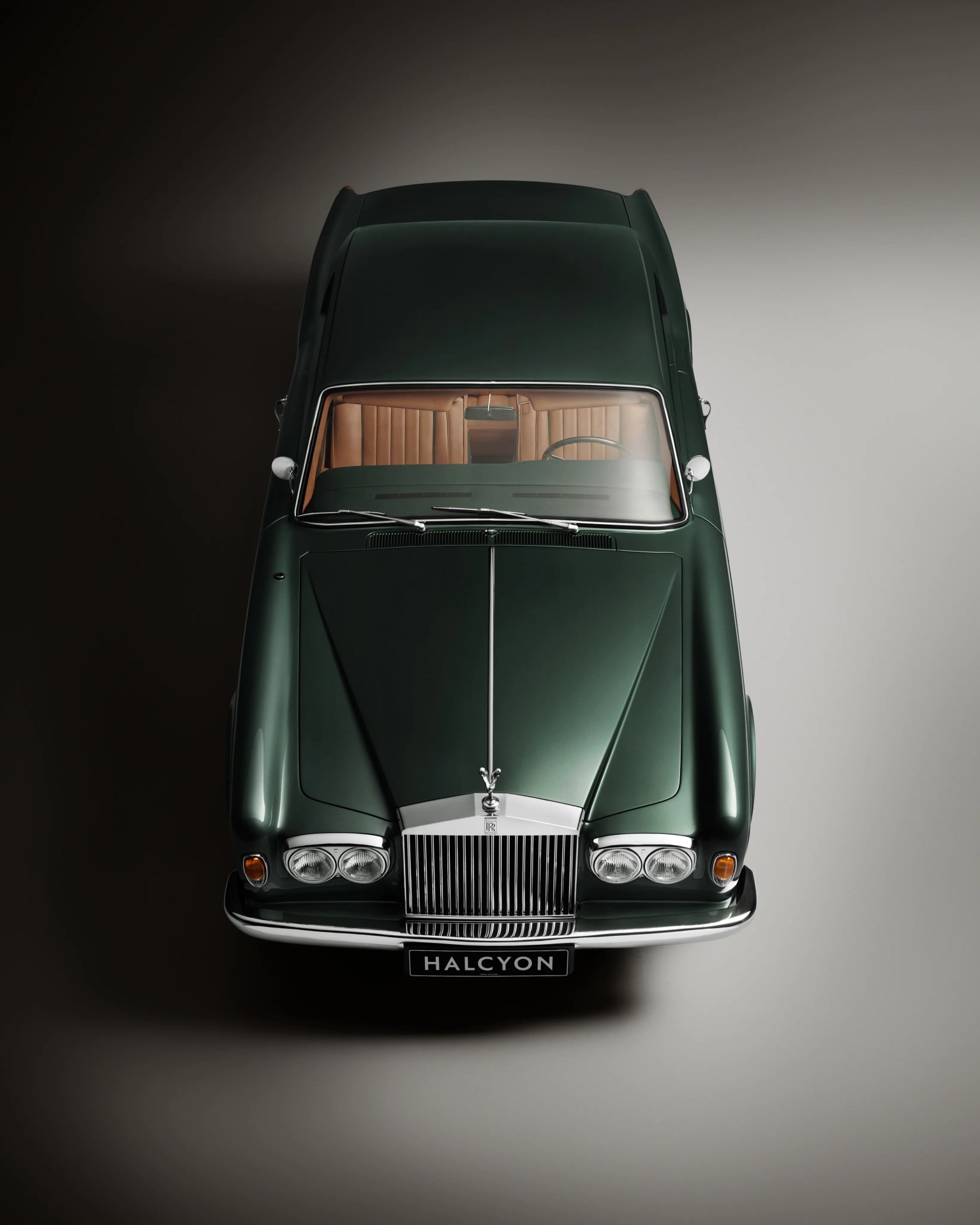 Dark green classic Rolls-Royce car with tan leather interior viewed from above on a gradient background.
