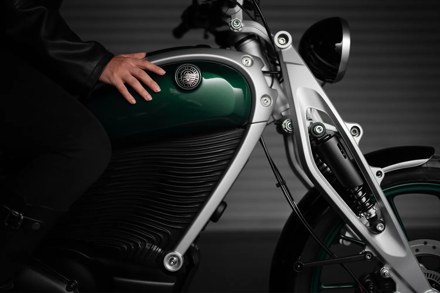 Close-up of a green and silver Royal Enfield motorcycle fuel tank and front suspension with a hand resting on the tank.