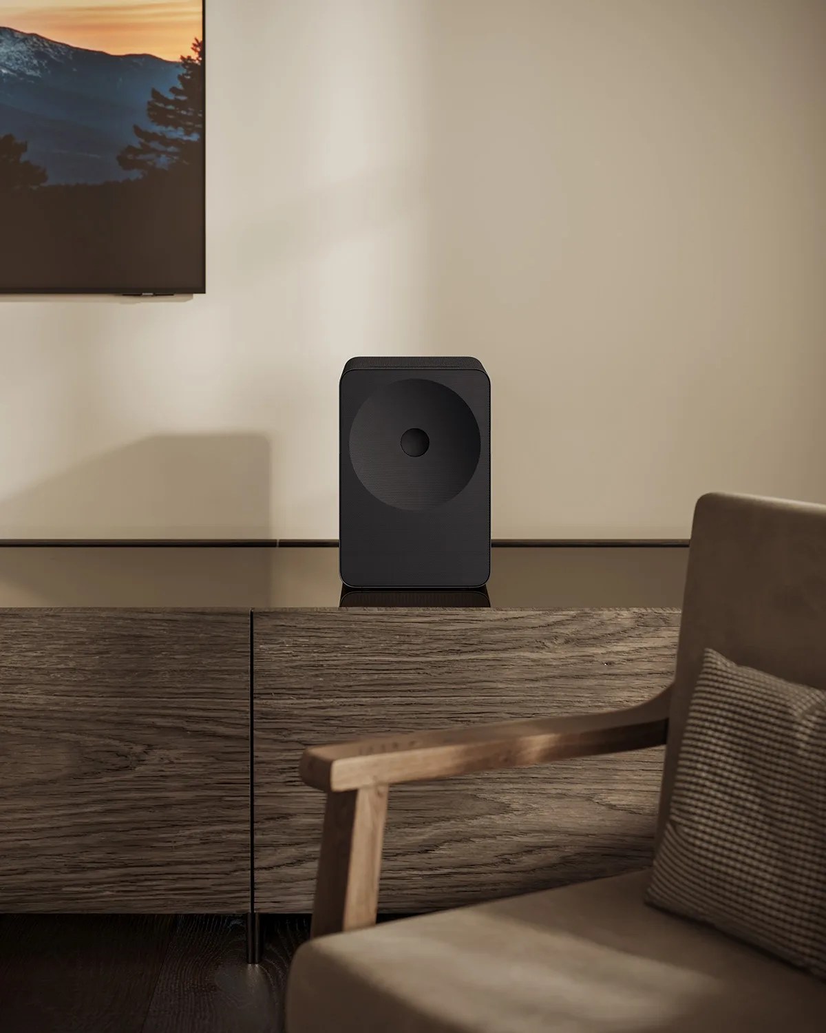 Black rectangular speaker with circular front grille on a wooden cabinet in a living room.
