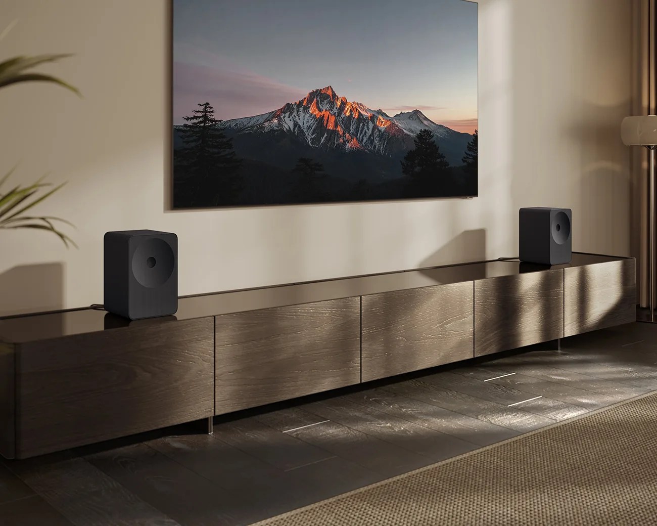 Modern living room setup with a wall-mounted TV displaying a mountain scene and two black speakers on a long wooden media console.