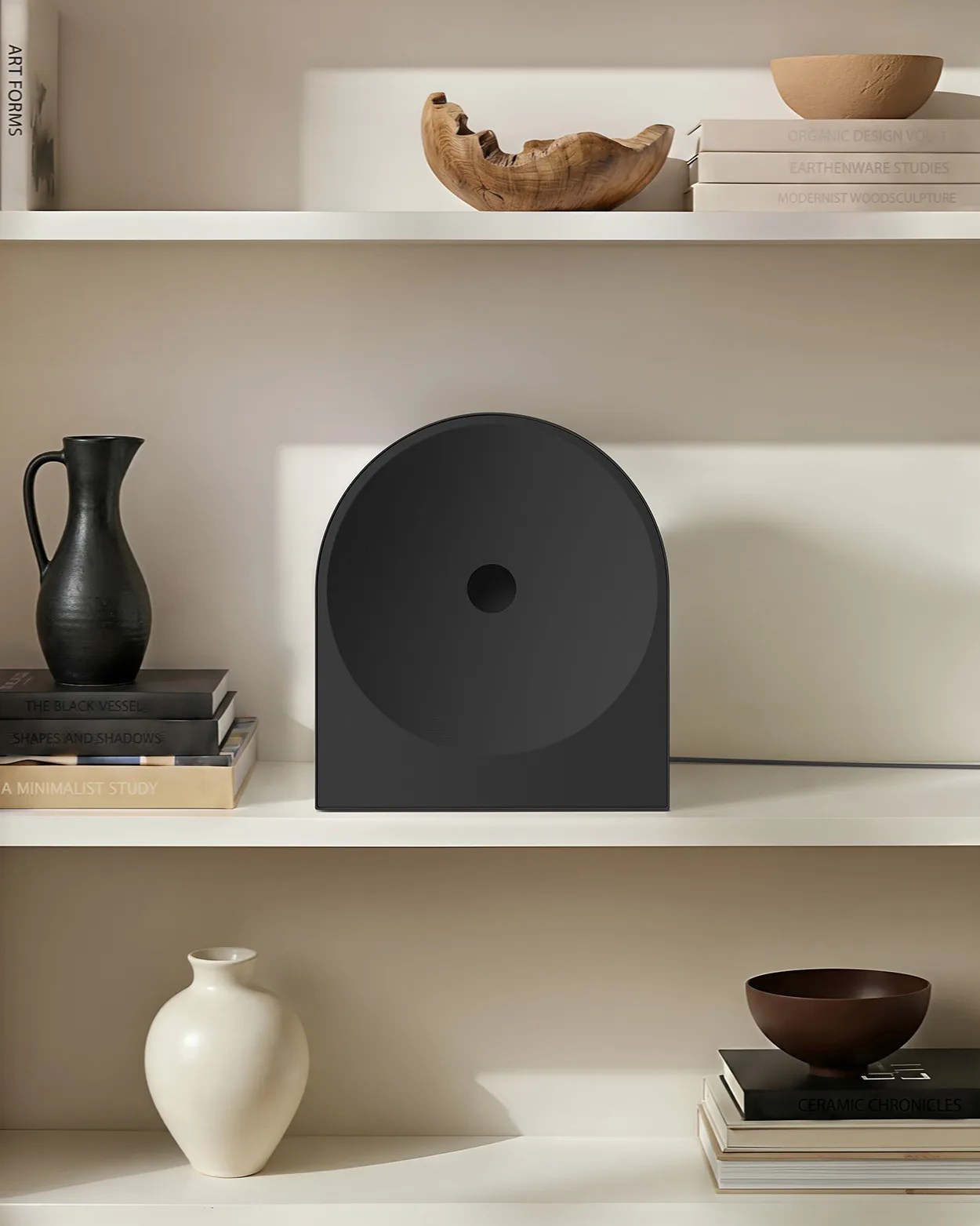 Matte black modern speaker with a circular front and a small central hole on a white shelf.
