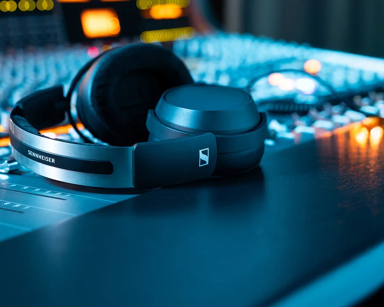 Black Sennheiser over-ear headphones resting on a sound mixing console with blurred lights in the background.