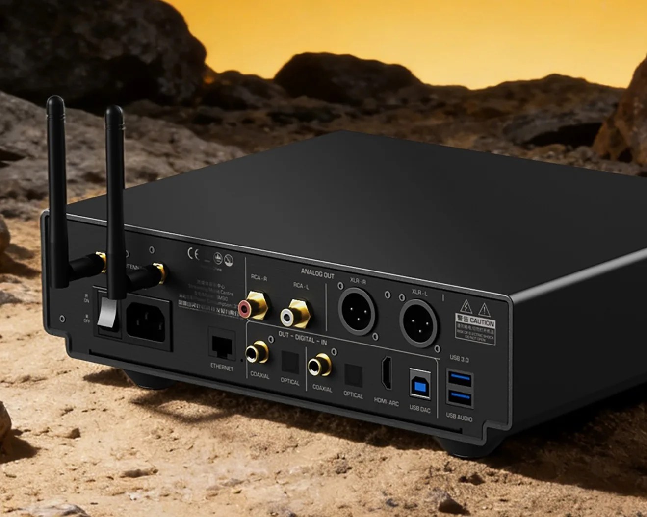 Black audio device with dual antennas, multiple analog and digital output ports, USB 3.0, and Ethernet on a rocky surface.
