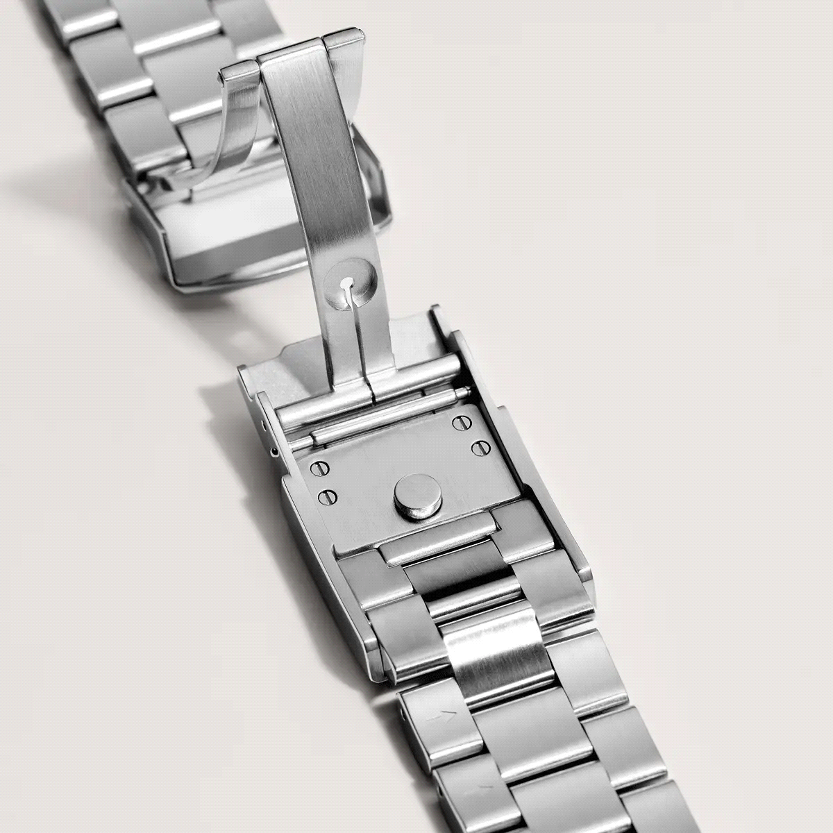 Close-up of a stainless steel watch band clasp with a folding deployment mechanism on a light background.